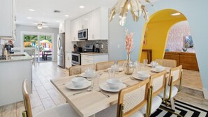 Une cuisine moderne avec des meubles blancs, un coin repas doté d’une table et de chaises en bois, et un mur d’accent jaune.