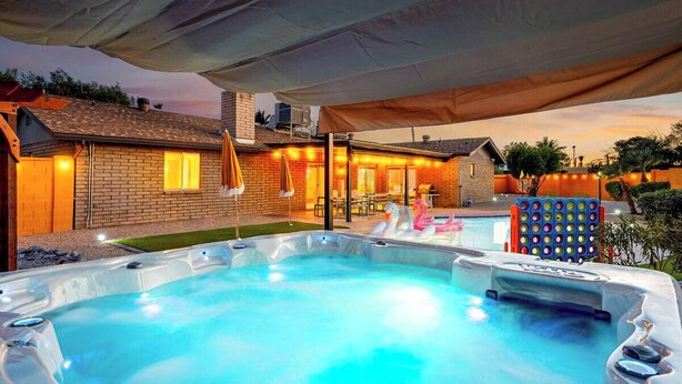 Un espace avec un jacuzzi, une terrasse couverte, une maison en briques et une piscine en arrière-plan.
