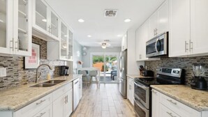 Une cuisine moderne avec des armoires blanches, des comptoirs en granit, un four à micro-ondes, une cuisinière et un mixeur.