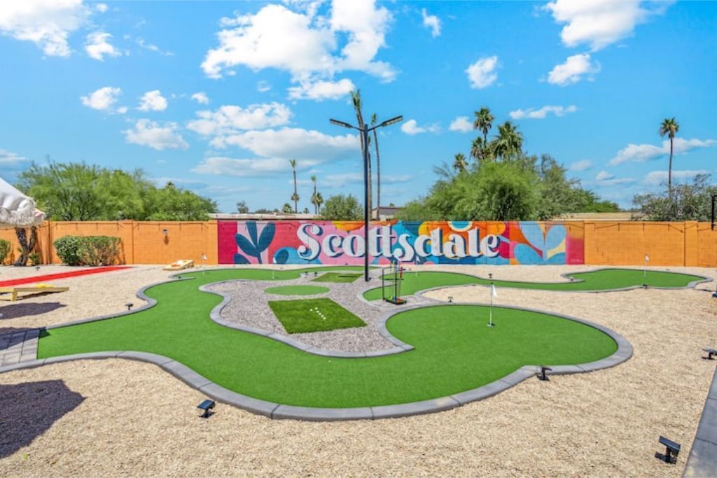 A miniature golf course with a colorful mural in the background and a clear sky.