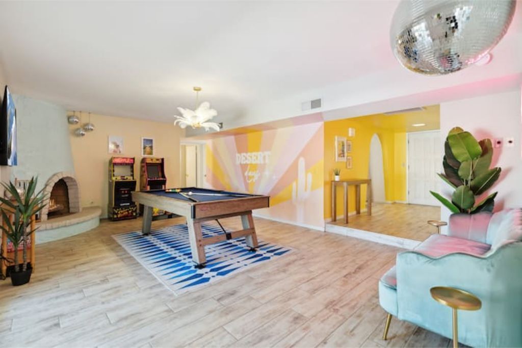 A pool table in a room with a yellow and white wall, a disco ball, and a blue sofa.