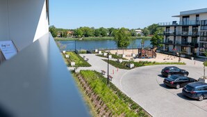 A view of a modern building with a parking area, a lake, and a playground. - Apartment with river view, sauna and indoor pool (Dziwnow)