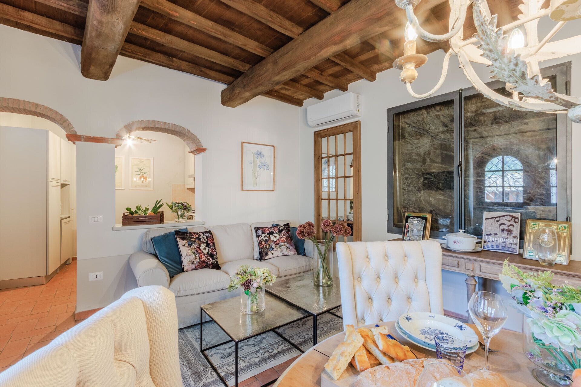 Un salon chaleureux avec un haut plafond en bois, une cheminée et un coin repas où une table est dressée pour le repas.