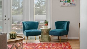 Um quarto com duas poltronas verde-água, um tapete estampado e uma pequena mesa redonda com uma planta.