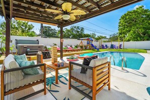 Un'area esterna coperta con piscina, sedie a sdraio, un'area giochi e una ventola a soffitto.