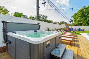 Una vasca idromassaggio con un pontile in legno, uno scivolo e una piscina in un giardino.