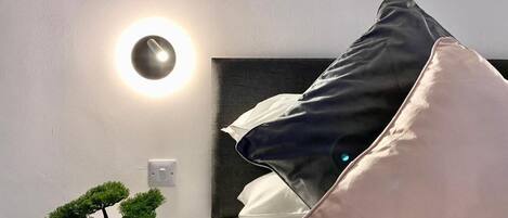 A neatly arranged hotel room with a bed, pillows, a bedside table with a bonsai tree, and a wall-mounted light fixture.