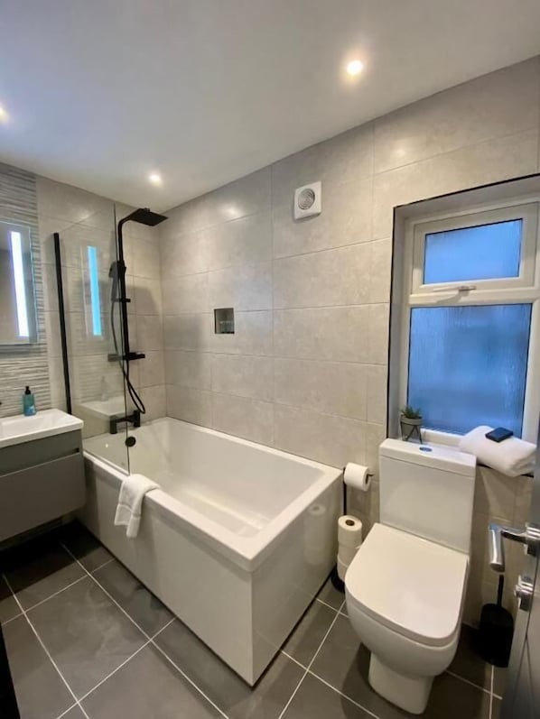 A modern bathroom with a freestanding bathtub, a toilet, and a sink. - Eden Retreats Serviced Apartments (Morecambe)