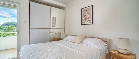 A bedroom with a bed, a nightstand, a lamp, a mirror, and a door leading to a balcony.