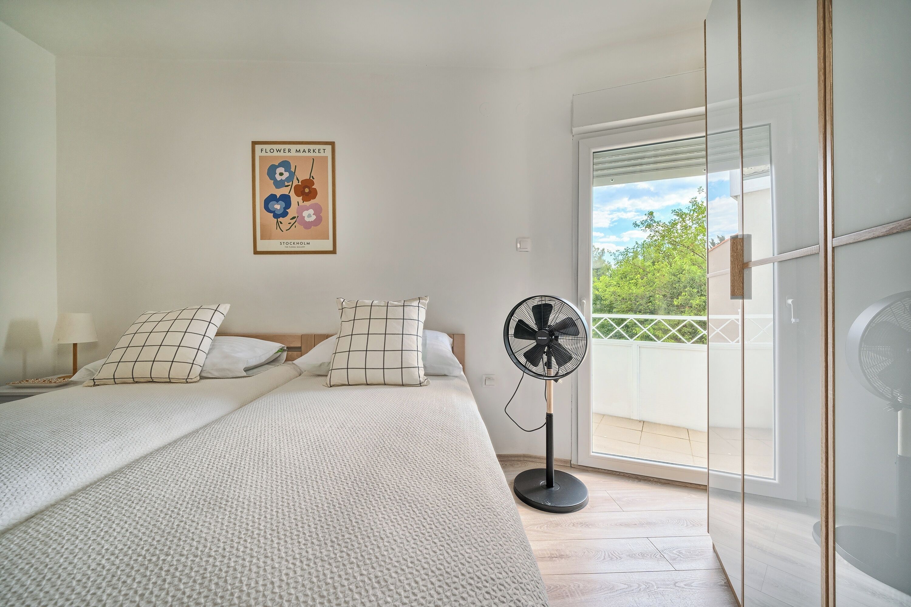 A bedroom with a bed, pillows, a fan, a poster, and a balcony.