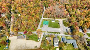 An aerial view of a lakeside property with a tennis court, a boat dock, and a sandy beach area.