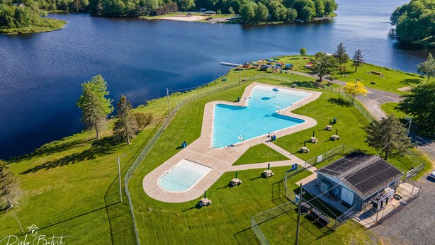 An aerial view of a swimming pool complex with a large central pool, a smaller adjacent pool, and a covered area with a roof.