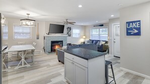 A modern kitchen with a central island, a dining area with a white table, and a living area with a fireplace.