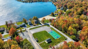 An aerial view of a lakeside residential area with houses, a basketball court, and a parking lot.