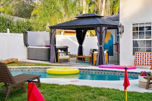 A backyard with a swimming pool, a gazebo, a dining area, and a children's play area.