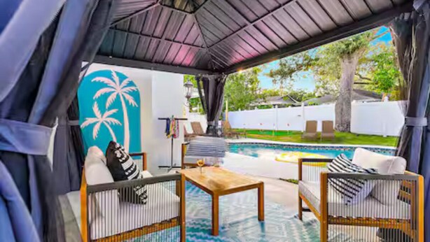 Un espacio de estar al aire libre techado con piscina, una mesa de madera y dos sillas de mimbre.