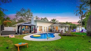 Una casa con piscina, mobiliario de exterior y un patio cubierto.