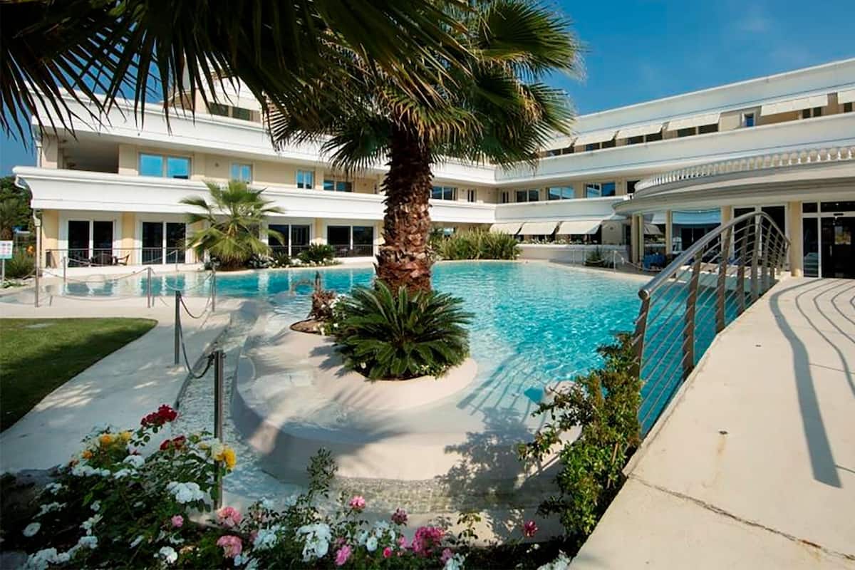 A pool area with a palm tree, a covered walkway, and a building with multiple windows.