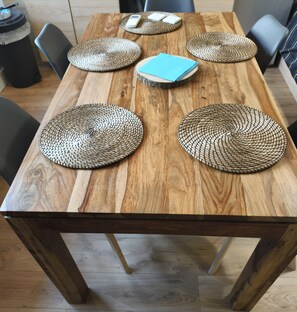 A wooden dining table with woven placemats, a blue folder, and chairs.