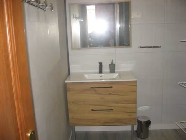 A bathroom with a wooden vanity, a sink, a mirror, and a trash can.