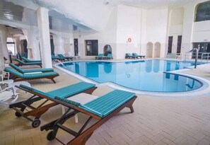 An indoor swimming pool with lounge chairs and a tiled floor.