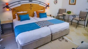A double bed with a wooden headboard, two blue pillows, and a checkered blanket. There is a small round table with a plant and two chairs. - Yasmine Beach - Families and Couples (Hammamet)