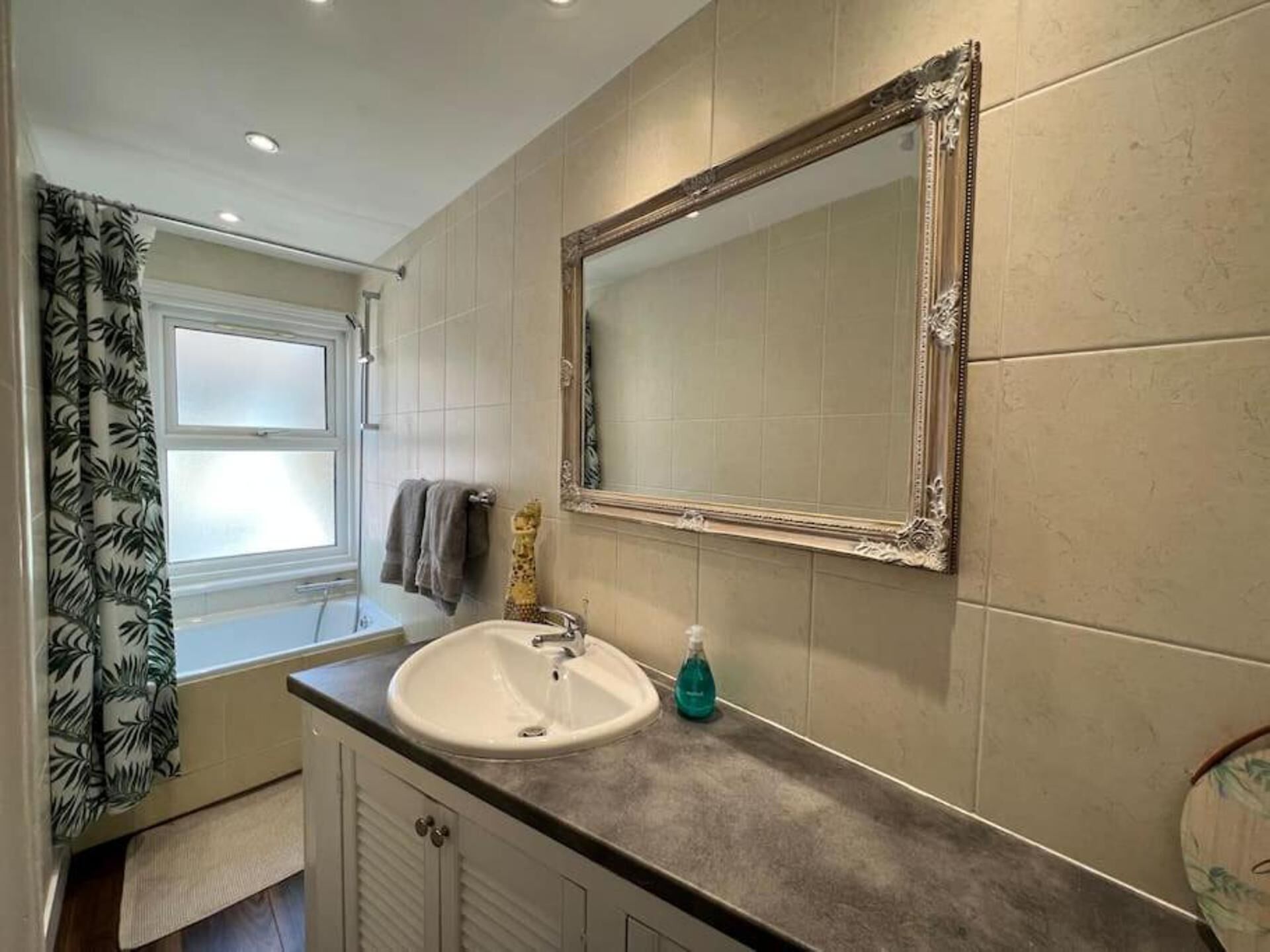 Une salle de bain avec un lavabo blanc, un miroir et une fenêtre avec un rideau.