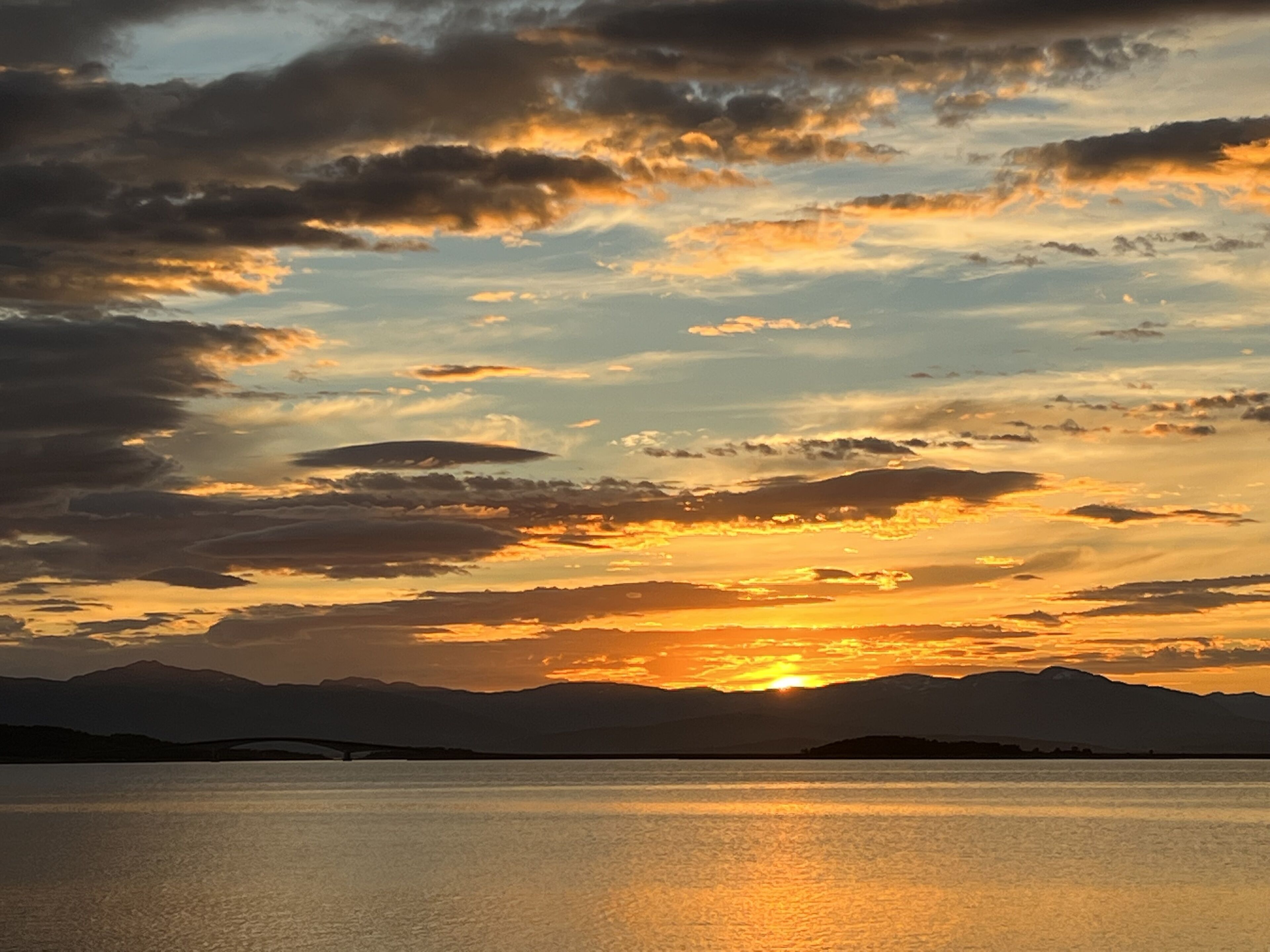 A sunset over a calm body of water with mountains in the background.