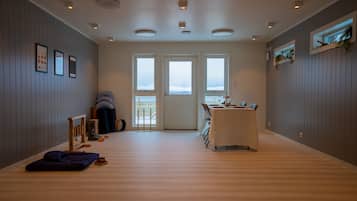 Una habitación amplia con suelo de madera, una mesa de comedor con sillas, una pequeña zona de estar con cojines y vistas a través de la puerta.