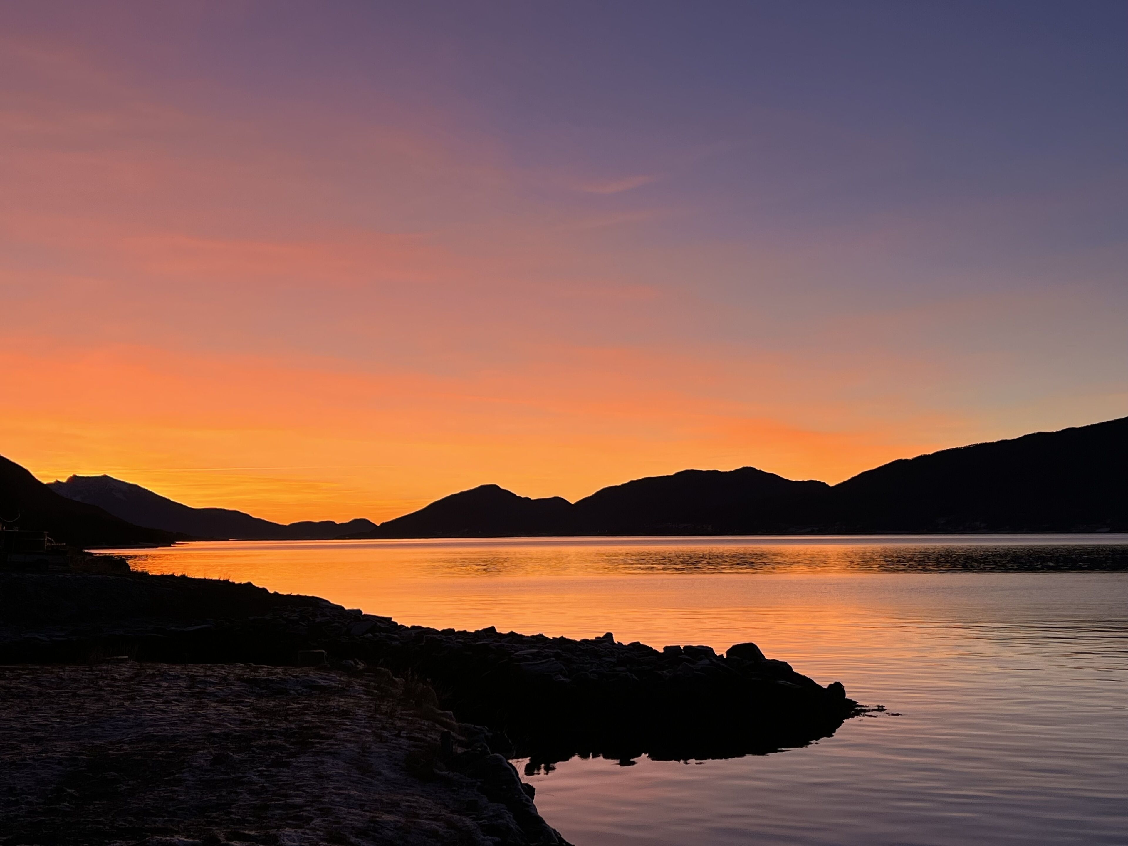 A serene lakeside view with mountains in the background during sunset.