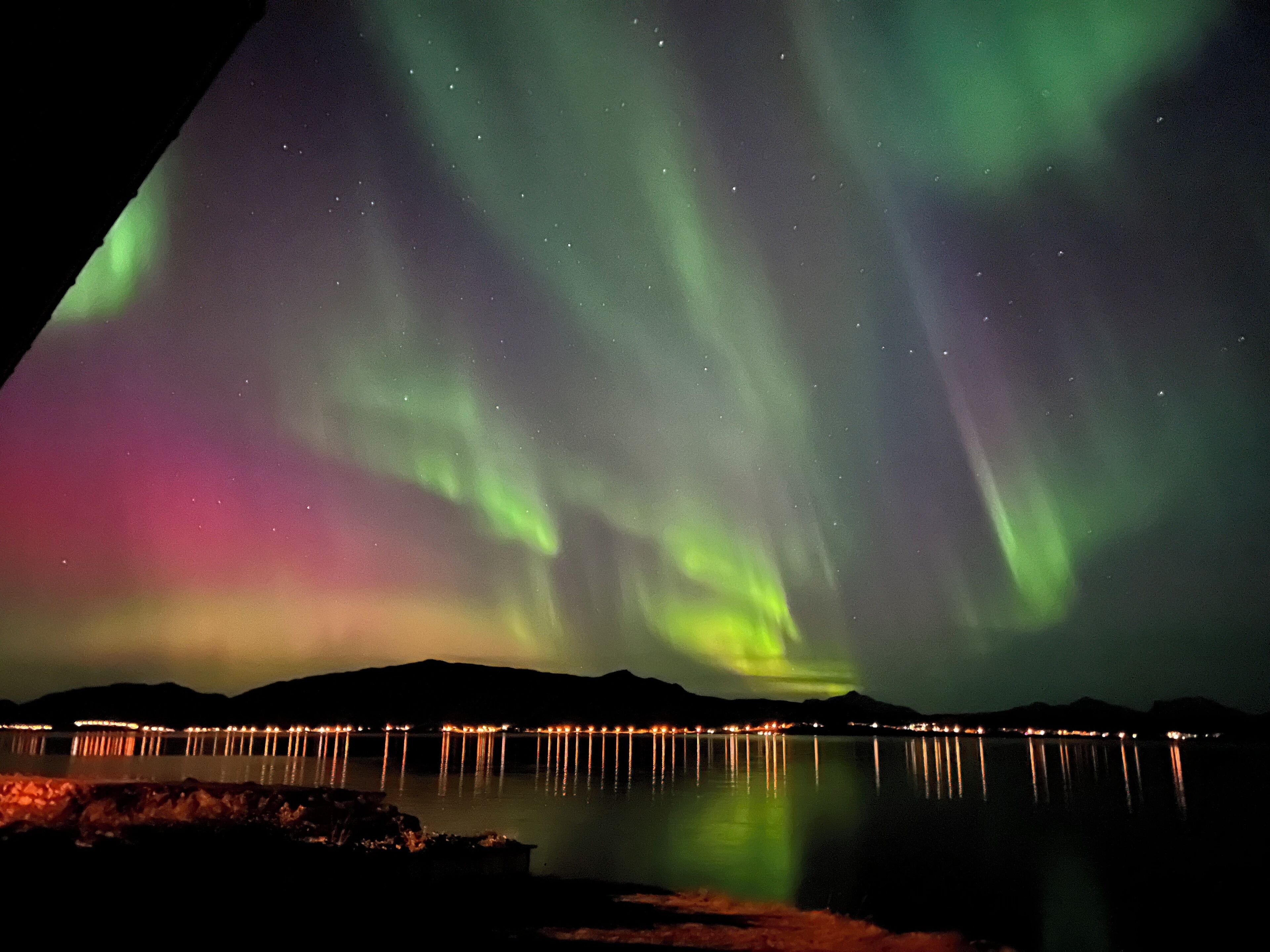 Vista nocturna de las auroras boreales sobre un lago tranquilo con un muelle iluminado.