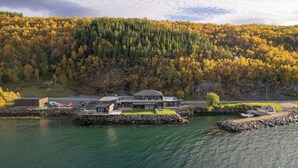 Un albergue junto al lago con un muelle, un edificio grande con techo plano y un promontorio boscoso al fondo.