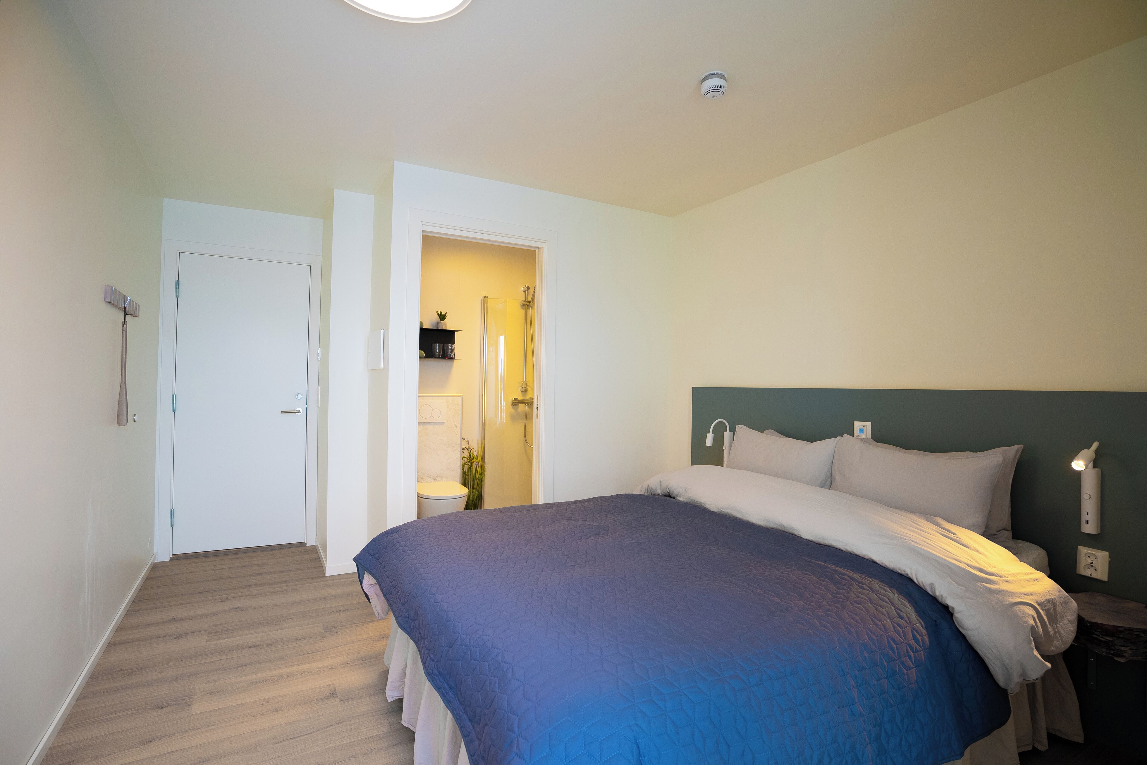 A bedroom with a large bed, a door leading to a bathroom, and a small table with a lamp.