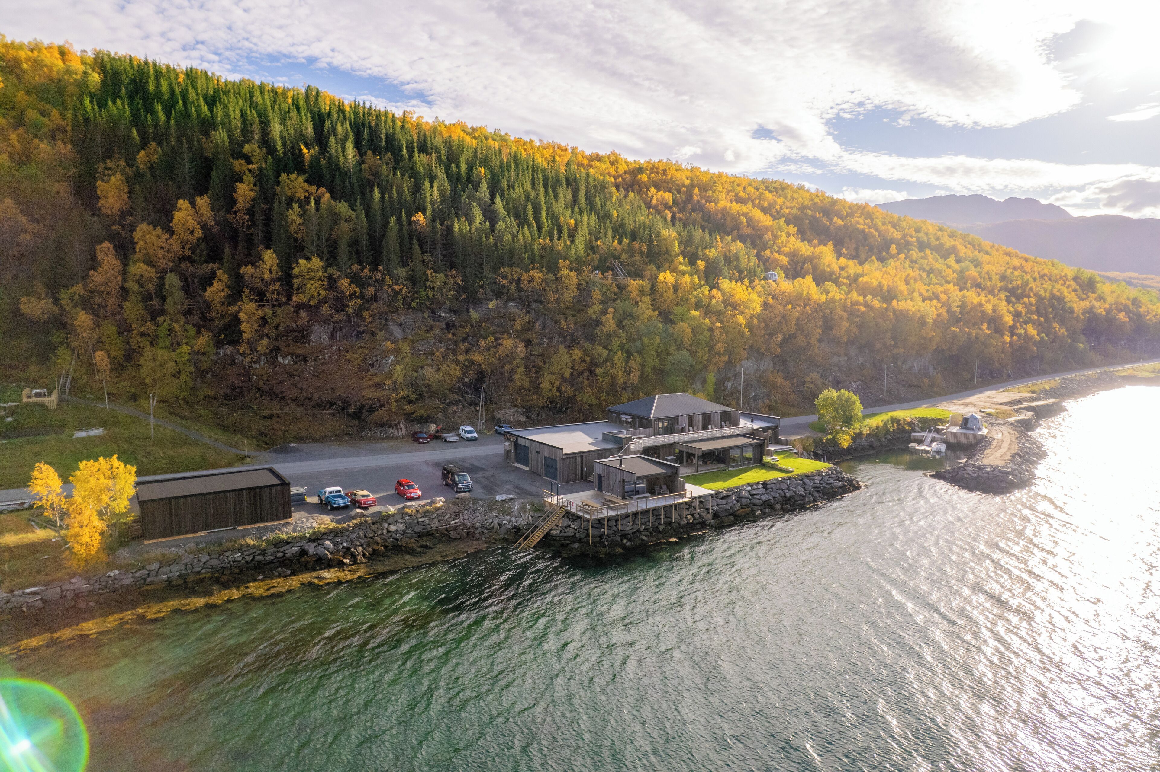 A waterfront property with a dock, a building with a large deck, and a forested hillside.