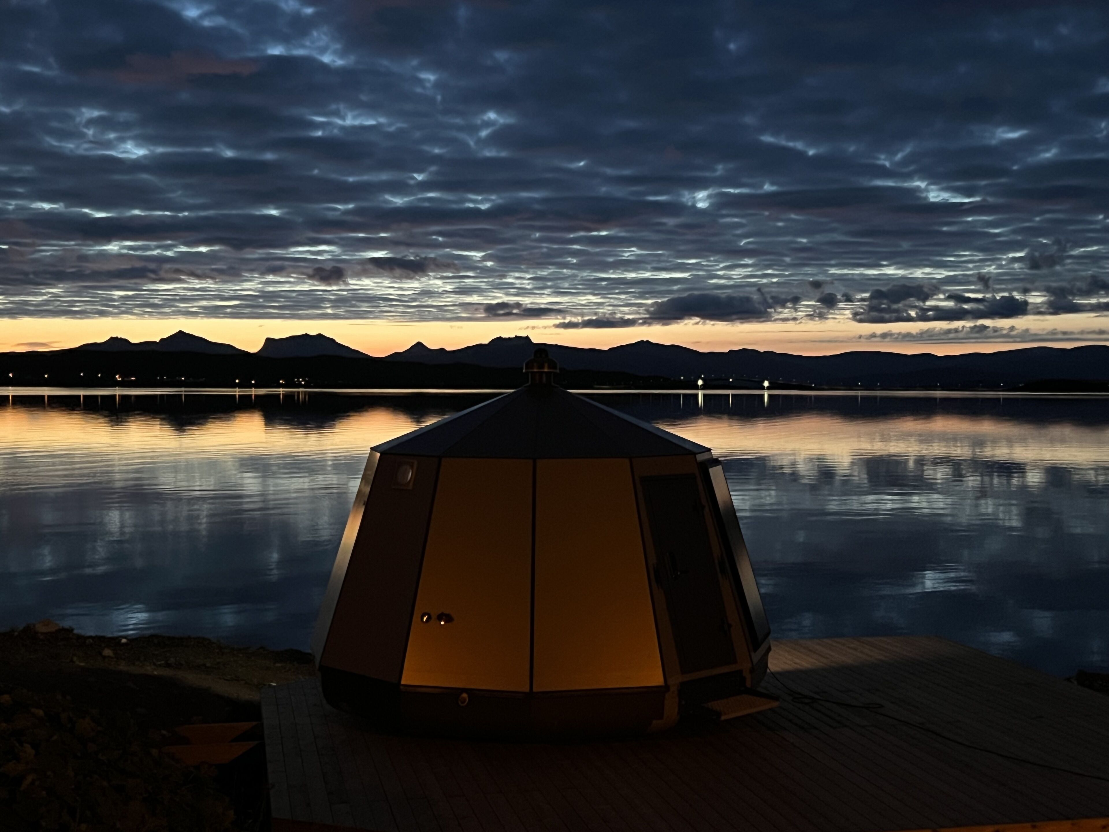 A gazebo on a wooden deck overlooking a calm lake with mountains in the background.