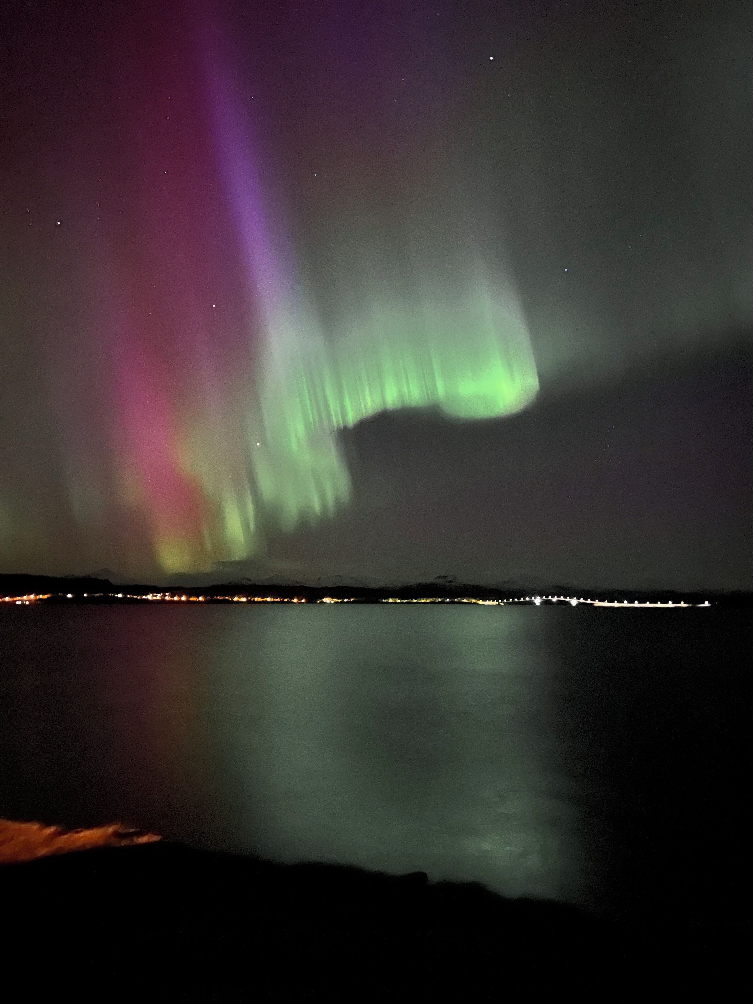 A night view of a coastal area with a visible aurora display over the water.