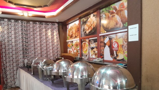 Montaje de bufé con estaciones de comida cubiertas y un cartel con el menú al fondo.
