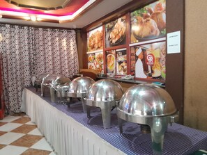 Montaje de bufé con estaciones de comida cubiertas y un cartel con el menú al fondo.