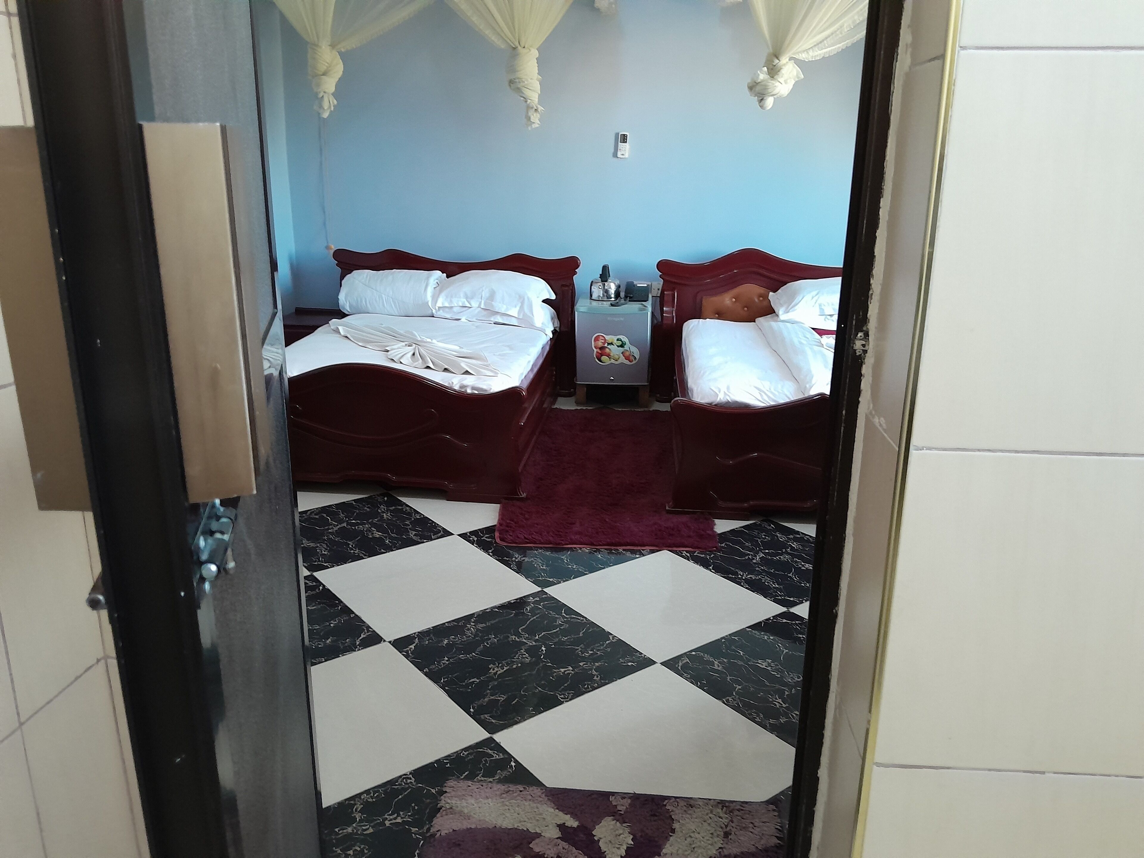 A hotel room with two beds, a checkered floor, and a nightstand with a lamp.