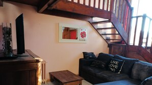 Una sala de estar con una mesa de centro de madera, un sofá negro con cojines estampados y un cuadro enmarcado en la pared.