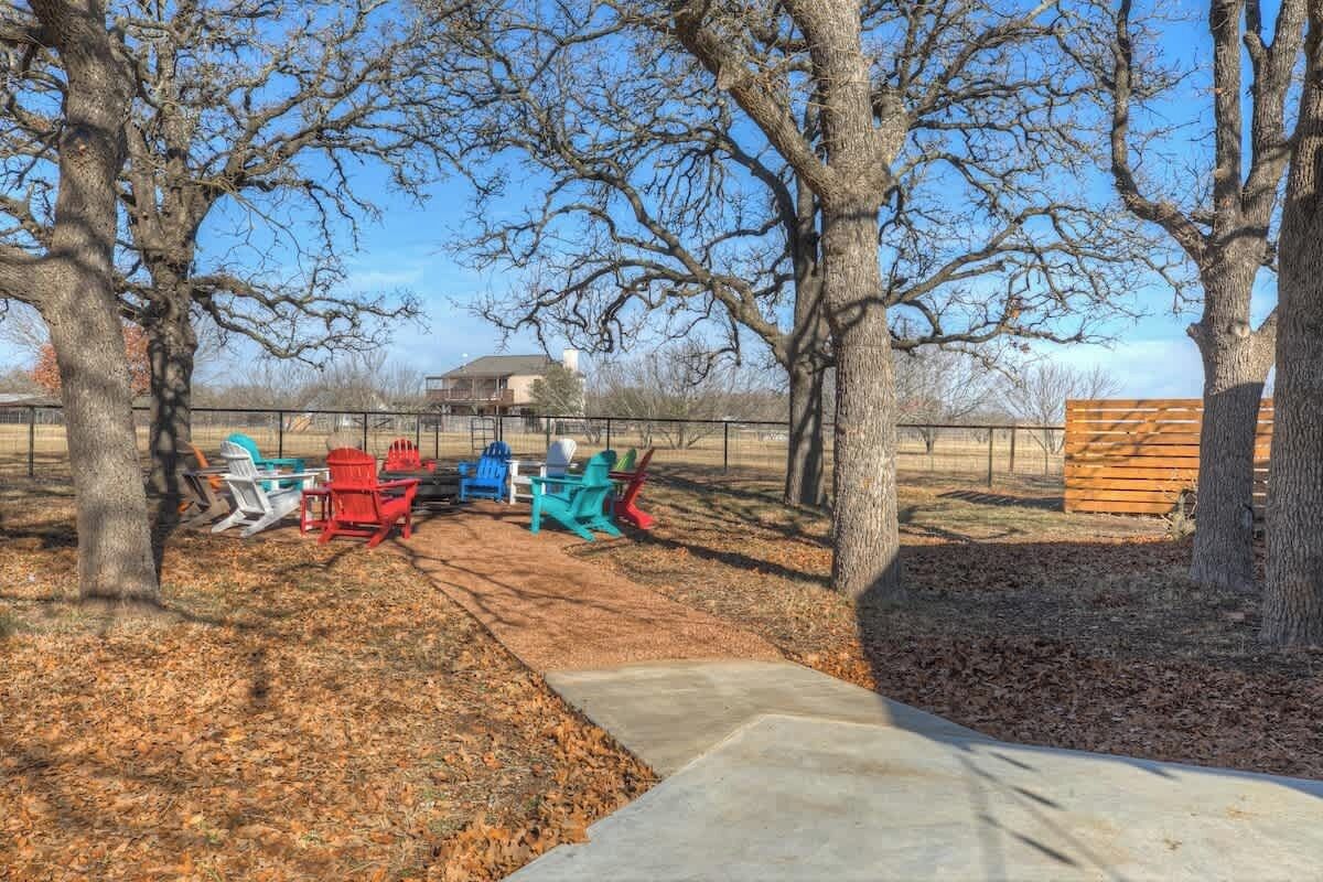 A park with trees, a concrete path, and colorful Adirondack chairs.