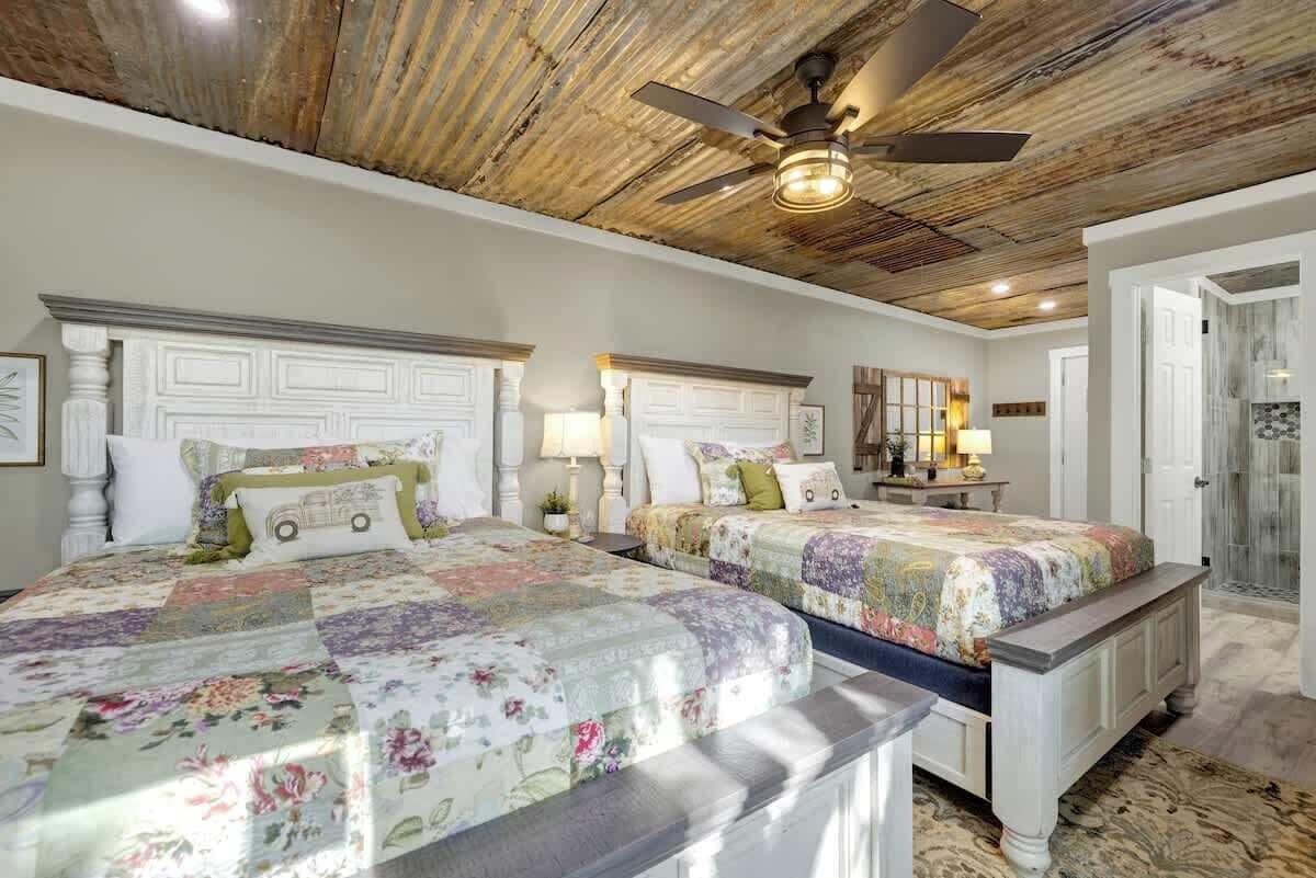Un dormitorio con dos camas, ventilador de techo y baño con ducha de vidrio.