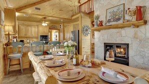 A wooden interior with a dining table set for a meal, a fireplace, and a clock on the wall.