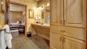 A wooden cabin interior with a bathroom, a bed, and a small seating area.