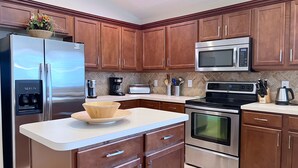 A modern kitchen with wooden cabinets, stainless steel appliances, and a white countertop. - Private Pool Oasis! No Rear Neighbors! VALUE RATE! (Davenport)