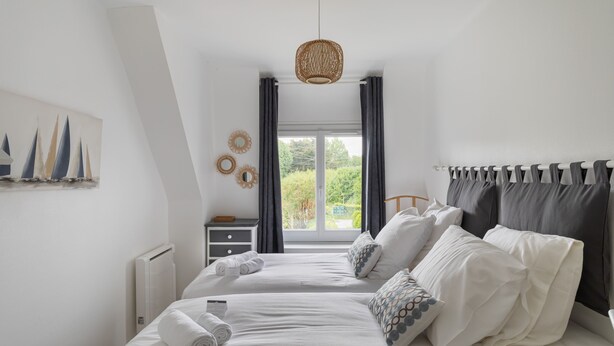 Une chambre moderne avec deux lits, une grande fenêtre et une vue sur la verdure.