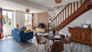 Un vaste espace de vie comprenant un canapé bleu, une table à manger en bois pour quatre personnes et un escalier avec des rampes en bois.