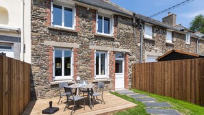 Une maison en pierre avec une terrasse en bois et un petit espace patio.