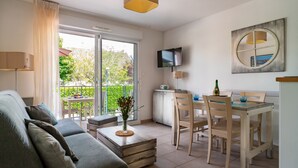 Una sala de estar moderna con sofá, una mesa de comedor con sillas, un televisor montado en la pared y un gran ventanal con cortinas.