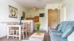 Un espacio habitable compacto con comedor, kitchenette y un sofá gris con cojines.